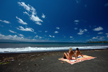 Couple sitting on black sand beach, Tahiti French Polynesia