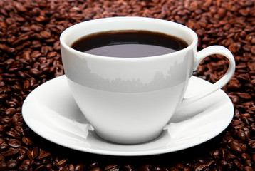 cup of coffee sitting in a bed of coffee beans isolated