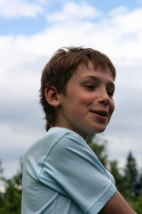 A smiling teenager half-turned on a background of clouds