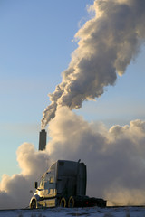 Fototapeta na wymiar A semi truck driving in front of a power plants smoke stack