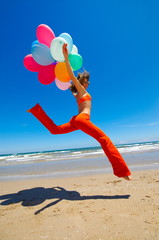young woman with colorful balloons jumping on the beach