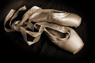 Worn ballet pointe shoes on a dark background.