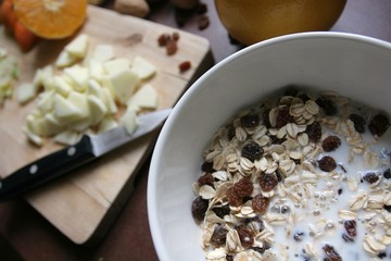 Preparation of a Bircher Muesli with fresh fruits and hazelnuts in a morning light atmosphere taken on a kitchen table.