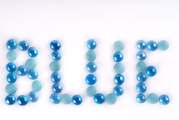 The word BLUE created and written by blue and turquoise glass stones on white background.