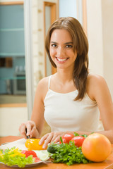Obraz na płótnie Canvas Young happy woman making salad at domestic kitchen