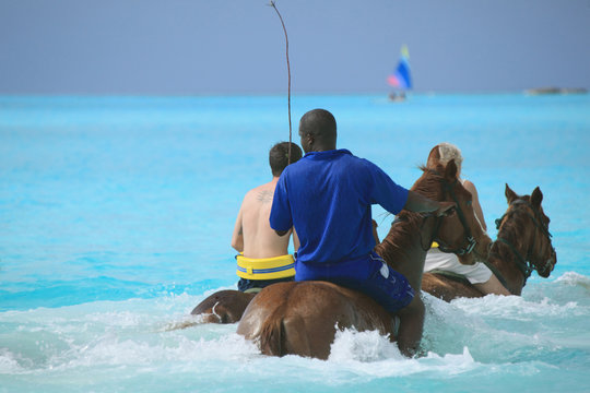 People horseback riding in tropical island beach ocean
