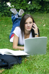 Cute teen girl on the phone laying down on the grass studying