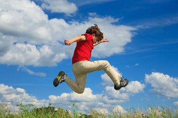 Kid running, jumping on green meadow against blue sky