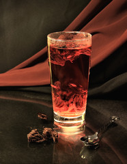 Glass with hot red tea on a background of a drapery.