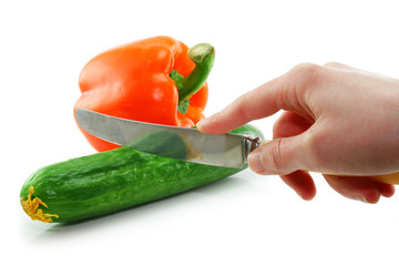 Woman's hand cuting green cucumber and orange paprika isolated