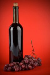 bottle of wine and grapes over red background