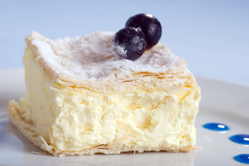 custard cake square on a plate with blueberries on blue