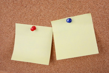 two yellow memo sticks with pins on cork board