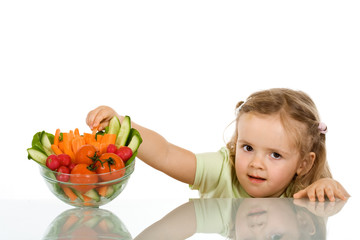Little girl stealing a vegetable from a bowl