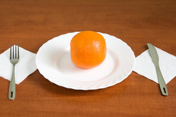 fresh oranges on a plate with knife and fork over wooden backgro