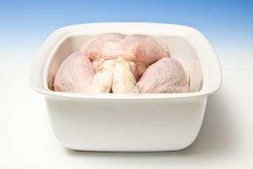 Whole raw chicken in a roasting dish on a blue studio background