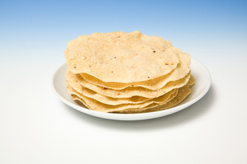 Plate of fresh pappadums on a blue studio background.