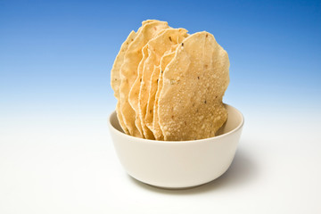 bowl of Pappadums on a blue studio background.