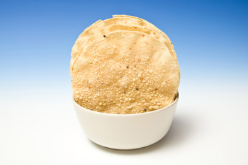 bowl of Pappadums on a blue studio background.