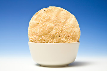 bowl of Pappadums on a blue studio background.