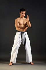 Young sporty karate man doing special exercise on gray backgroun
