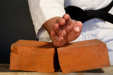Young sporty karate man breaking three bricks on gray background © Andrey Ushakov