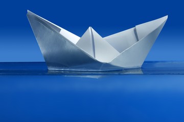 Obraz premium Paper boat floating over blue real water