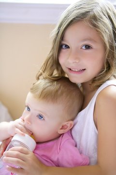 Toddler girl giving bottle of milk to baby sister