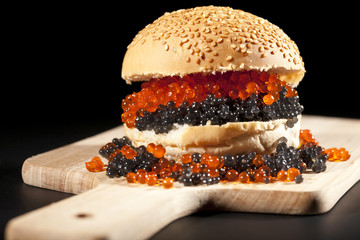 big hamburger with red and black caviar on black background