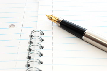 A gold-nibbed pen on a spiral-bound notepad