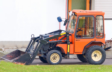 Orange tractor with scoop bucket in the suburbs