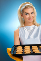 Beautiful woman holding hot roasting pan with oat cookies on it.
