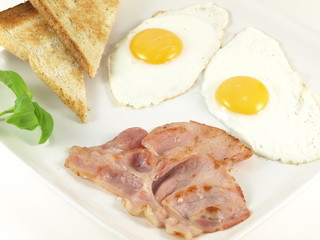 Fried eggs, bacon, toasts and basil on a plate.