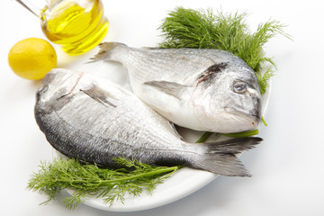 Couple of raw sea breams in white plate with ingredients