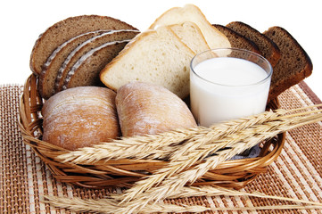 Rolls, bread and a glass of milk in a basket on a table