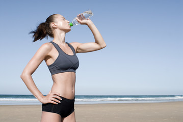 Sportliche junge Frau trinkt am Strand
