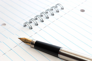 A gold-nibbed pen on a spiral-bound notepad