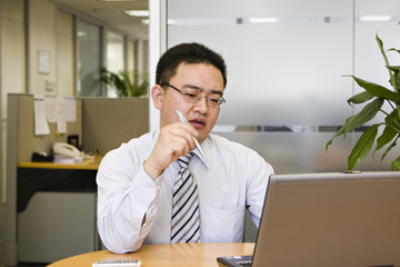 asian businessman thinking while looking at computer screen
