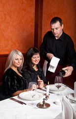 The waiter pours wine into the glass. Girls look.