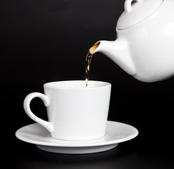 Pour tea from the teapot into the cup on a black background