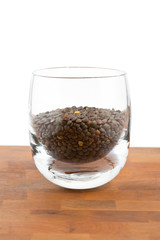 green lentils in glass on wooden table, white background