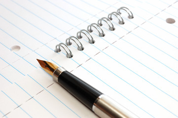 A gold pen on a spiral-bound notepad