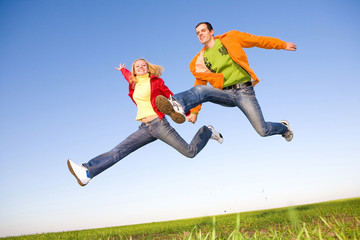 Happy young couple  jumping in sky above a green meadow