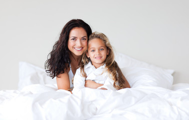 Mother and daughter on bed smiling at camera