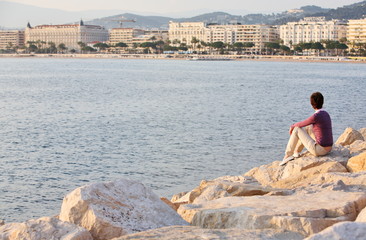 Fototapeta na wymiar Girl is resting on stones of pier with Cannes city background