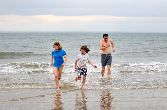 father and daughters running in the sea