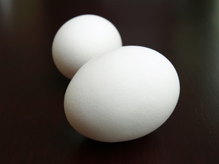 Two white eggs on a dark brown kitchen table