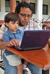 Hispanic father and son use the computer together