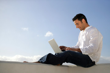 homme assis sur un mur avec ordinateur portable