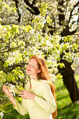 Beautiful red hair woman standing under blooming tree